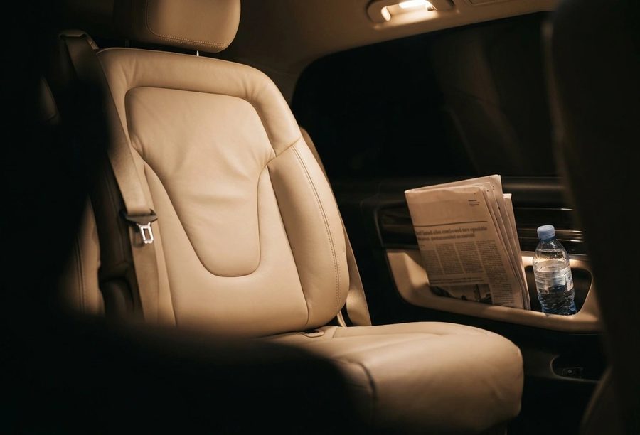 The rear cabin of a chauffeur car: cream leather seat, bottled water in the door pocket.
